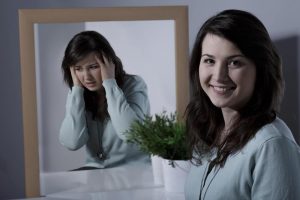 Mujer frente al espejo, viendose refleja como una mujer conmal humor, pero en realidad se encuentra sonriendo